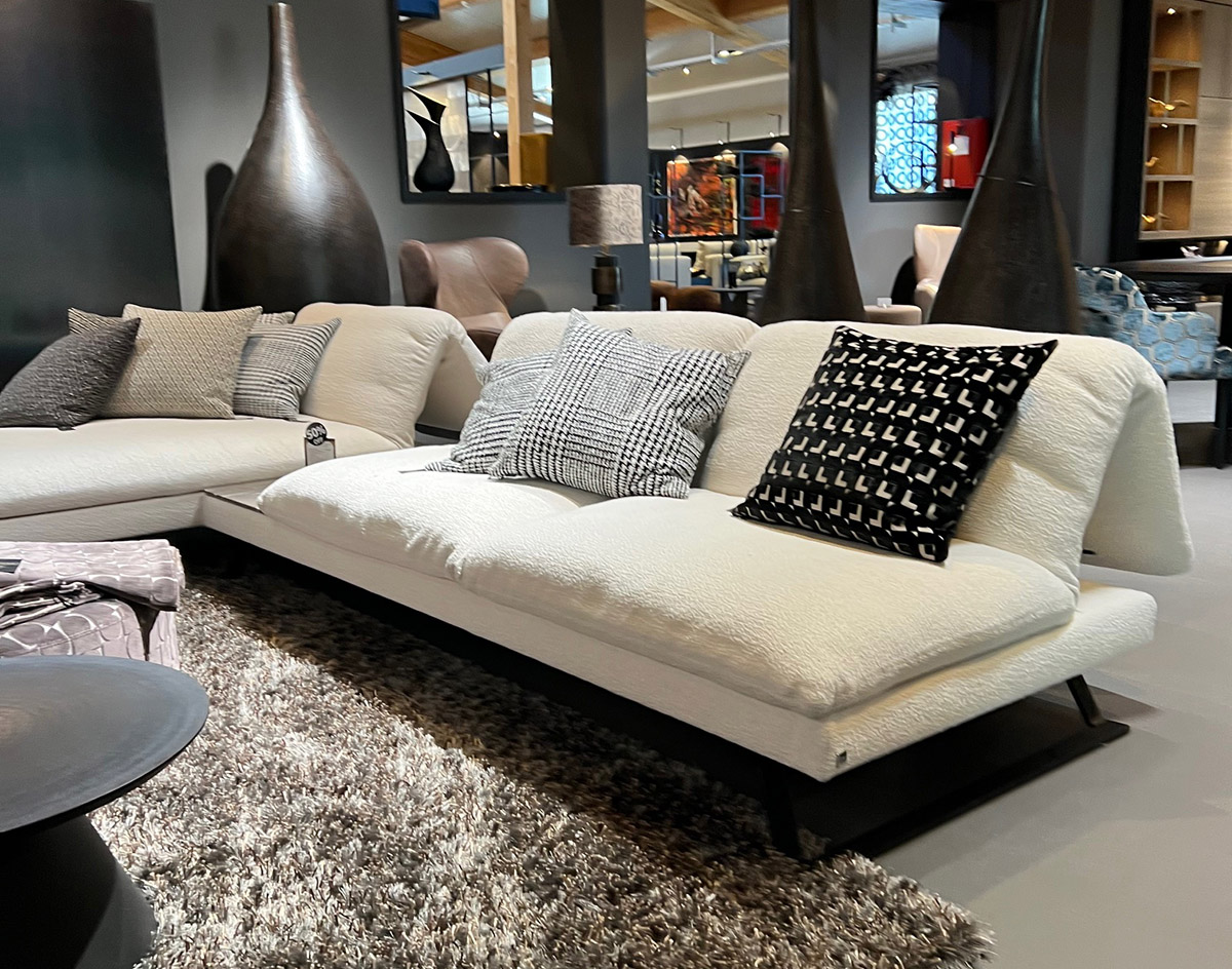 Weißes Sofa mit gemusterten Kissen in modernem Wohnzimmer, grauem Teppich und stilvollen Vasen.