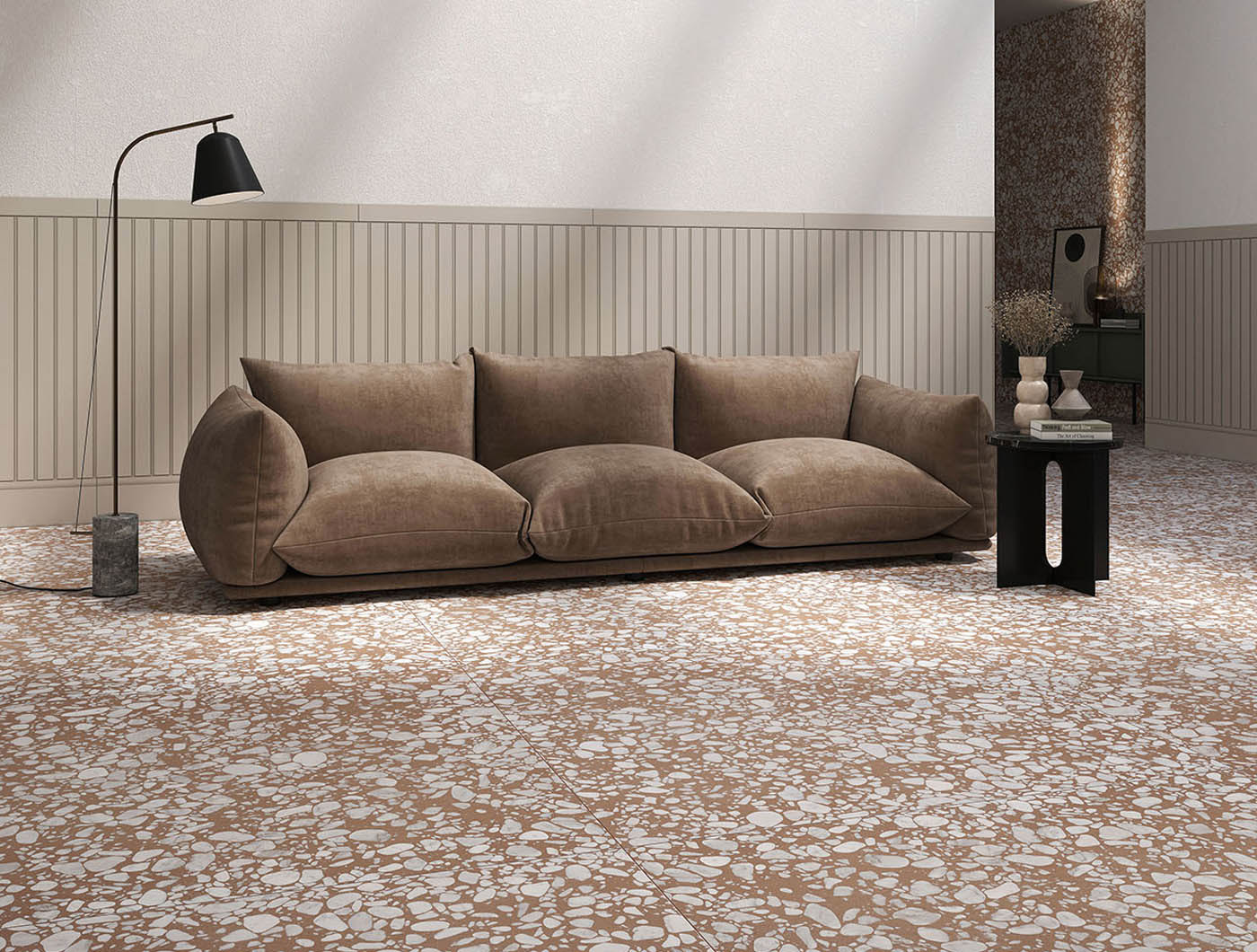 Ein gemütliches braunes Sofa mit neutralen Farben steht vor einer strukturierten Wand auf Terrassenfliesen