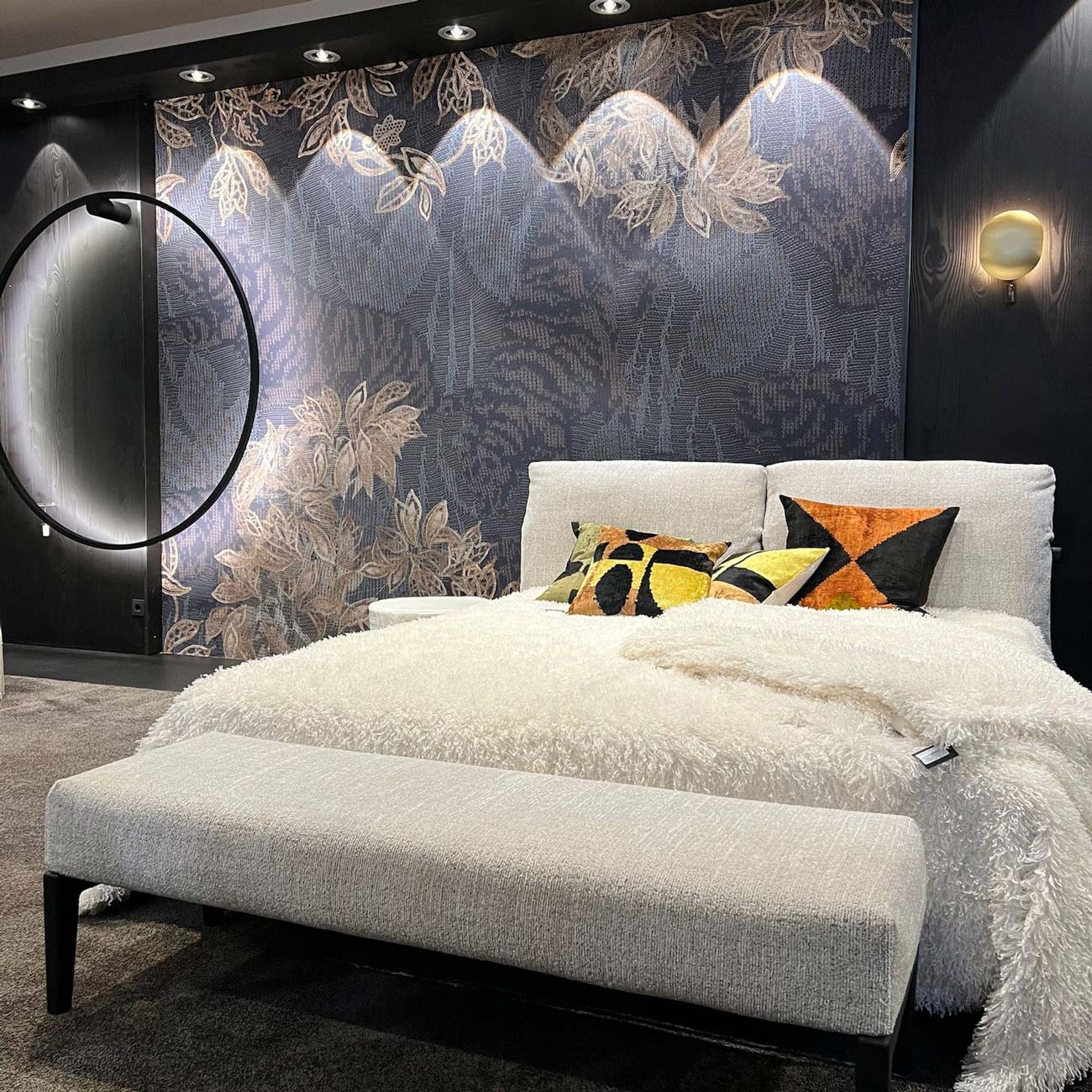 Elegantes Schlafzimmer mit grauem Bett runder Spiegel und floraler Tapete